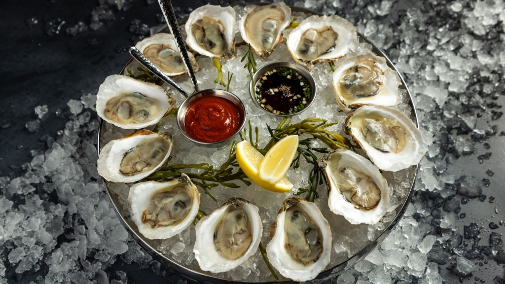 A circular plate of oysters over ice. In the middle of the circle are two dips, lemon and seaweed to garnish.